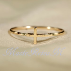 May include: A simple gold ring with a cross design. The ring is thin and delicate, and the cross is centered on the band.