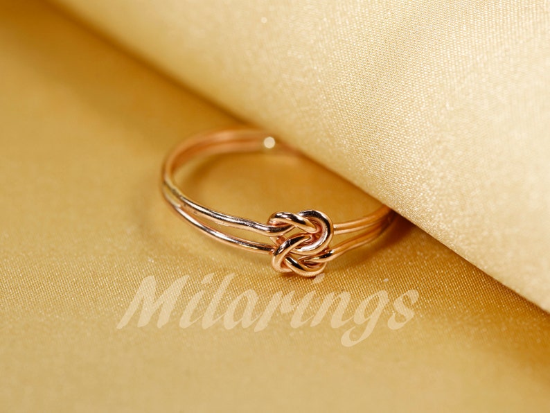 May include: A rose gold knot ring with a double band.
