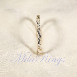 Peut inclure: Une bague argent&eacute;e avec un motif torsad&eacute; en forme de corde. La bague est pos&eacute;e sur un fond blanc cass&eacute;. Le texte "Mila Rings" est visible en bas de l'image.