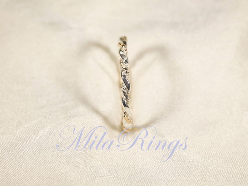 Peut inclure: Une bague argent&eacute;e avec un motif torsad&eacute; en forme de corde. La bague est pos&eacute;e sur un fond blanc cass&eacute;. Le texte "Mila Rings" est visible en bas de l'image.