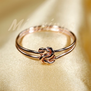 May include: A rose gold double knot ring. The ring is made of two bands of metal that are intertwined to form a knot.