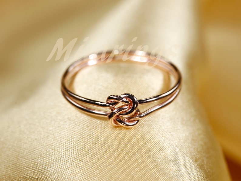 May include: A rose gold double knot ring. The ring is made of two bands of metal that are intertwined to form a knot.