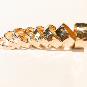 K&ouml;nnte beinhalten: Ein Satz von sieben goldfarbenen, geh&auml;mmerten Metallringen in verschiedenen Gr&ouml;&szlig;en. Die Ringe sind &uuml;bereinander gestapelt, wobei der gr&ouml;&szlig;te Ring oben und der kleinste Ring unten liegt.