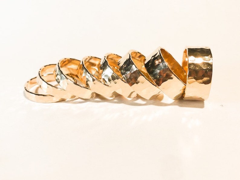 K&ouml;nnte beinhalten: Ein Satz von sieben goldfarbenen, geh&auml;mmerten Metallringen in verschiedenen Gr&ouml;&szlig;en. Die Ringe sind &uuml;bereinander gestapelt, wobei der gr&ouml;&szlig;te Ring oben und der kleinste Ring unten liegt.