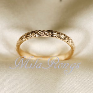 Op de afbeelding: Een dunne gouden ring met een delicaat bloemenmotief. De ring ligt op een witte stoffen achtergrond.