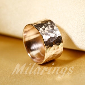 May include: A wide gold band ring with a hammered texture. The ring is made of metal and has a shiny finish.