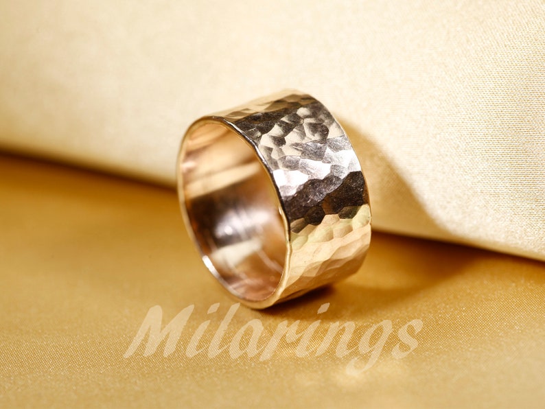 Op de afbeelding: Een brede gouden ring met een gehammerde textuur. De ring is gemaakt van metaal en heeft een glanzende afwerking.