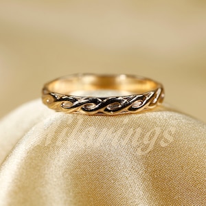 Könnte beinhalten: Ein goldener Ring mit geflochtenem Design. Der Ring liegt auf einem goldenen Stoffhintergrund.