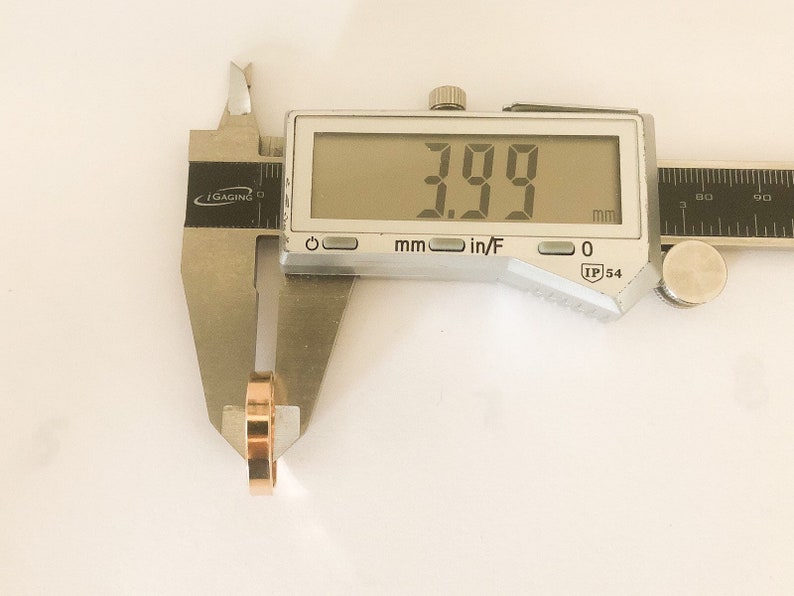 K&ouml;nnte beinhalten: Eine silberne digitale Schieblehre misst 3,99 mm. Die Schieblehre wird verwendet, um die Breite eines goldenen Rings zu messen.