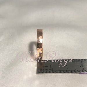 May include: A hammered rose gold band ring with a textured surface. The ring is measured against a ruler with markings in centimeters.