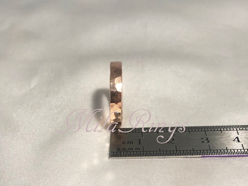 May include: A hammered rose gold band ring with a textured surface. The ring is measured against a ruler with markings in centimeters.