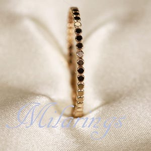 May include: Rose gold ring with a dotted design. The ring is set against a soft, off-white background. The ring's band is adorned with small, evenly spaced dots, creating a textured appearance. The ring is a delicate piece of jewelry.