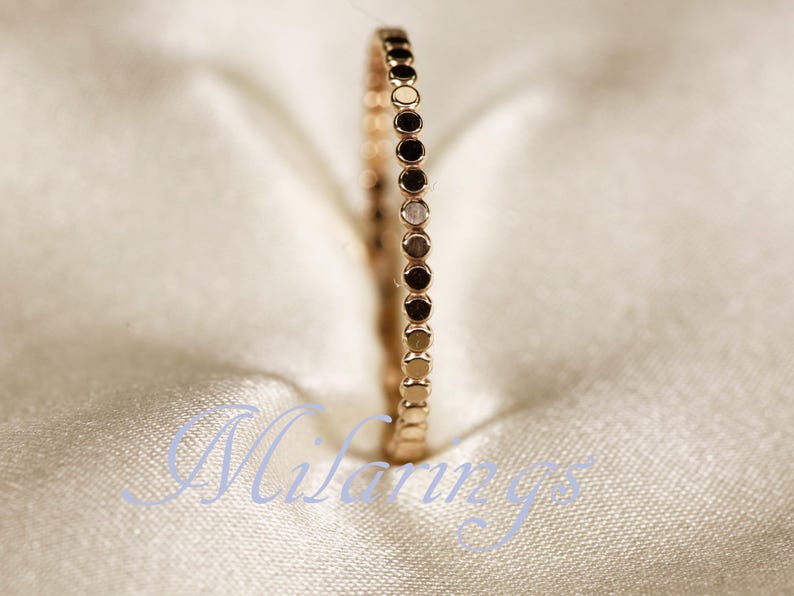 May include: Rose gold ring with a dotted design. The ring is set against a soft, off-white background. The ring's band is adorned with small, evenly spaced dots, creating a textured appearance. The ring is a delicate piece of jewelry.