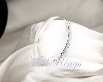 May include: A silver bangle bracelet with a textured design. The bracelet is on a white fabric background.