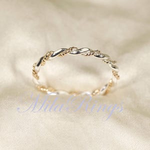 Peut inclure: Une bague torsad&eacute;e argent&eacute;e et dor&eacute;e. La bague pr&eacute;sente un motif tress&eacute; avec des sections argent&eacute;es et dor&eacute;es altern&eacute;es. La bague est pos&eacute;e sur un fond blanc cass&eacute;. Le texte "Nila Rings" est visible dans l'image.