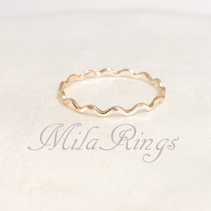 May include: A gold-toned ring with a wavy, textured band. The ring is on a white background.