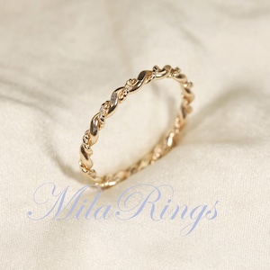 Peut inclure: Une bague dor&eacute;e avec un motif de corde torsad&eacute;e. La bague est en m&eacute;tal brillant et pr&eacute;sente un motif d&eacute;licat et entrelac&eacute;. La bague est un bijou, probablement pour le doigt, et est pr&eacute;sent&eacute;e sur un fond de tissu blanc. Le texte "Mila Rings" est visible.