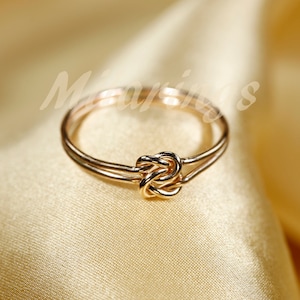 May include: A gold-toned ring with a knot design. The ring is made of two bands that are intertwined.