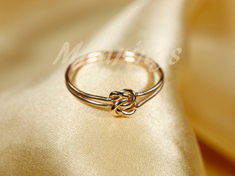 May include: A gold-toned ring with a knot design. The ring is made of two bands that are intertwined.