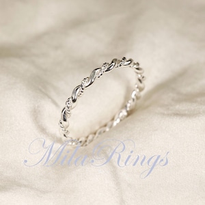 Peut inclure: Une bague argent&eacute;e avec un motif de corde torsad&eacute;e. La bague est pos&eacute;e sur un fond blanc cass&eacute; doux. Le design de la bague pr&eacute;sente une s&eacute;rie de brins entrelac&eacute;s, cr&eacute;ant un aspect textur&eacute; et &eacute;l&eacute;gant. C'est un bijou.