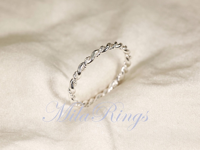Peut inclure: Une bague argent&eacute;e avec un motif de corde torsad&eacute;e. La bague est pos&eacute;e sur un fond blanc cass&eacute; doux. Le design de la bague pr&eacute;sente une s&eacute;rie de brins entrelac&eacute;s, cr&eacute;ant un aspect textur&eacute; et &eacute;l&eacute;gant. C'est un bijou.