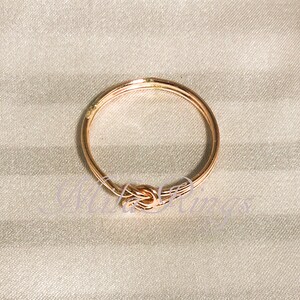 Op de afbeelding: Een ros&eacute;gouden ring met een knoopdesign. De ring is gemaakt van metaal en heeft een gepolijste afwerking.