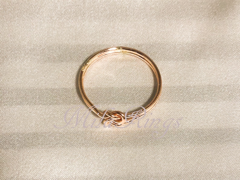 Op de afbeelding: Een ros&eacute;gouden ring met een knoopdesign. De ring is gemaakt van metaal en heeft een gepolijste afwerking.