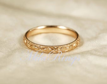 May include: A rose gold band ring featuring a continuous engraved floral pattern around the exterior surface. The metal has a polished finish with delicate milgrain detailing along the top and bottom edges of the band, creating a textured look.