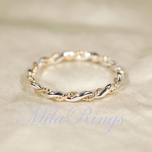 Op de afbeelding: Een tweekleurige ring met een gedraaid touwontwerp. De ring heeft afwisselende secties van zilver- en goudkleurig metaal, waardoor een gevlochten uiterlijk ontstaat. De ring is geplaatst tegen een zachte, neutrale achtergrond.