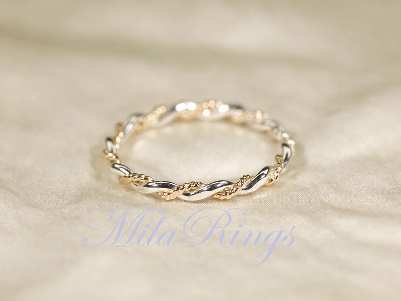 Peut inclure: Une bague bicolore avec un motif de corde torsad&eacute;e. La bague pr&eacute;sente des sections altern&eacute;es de m&eacute;tal argent&eacute; et dor&eacute;, cr&eacute;ant un aspect tress&eacute;. La bague est pos&eacute;e sur un fond doux et neutre.