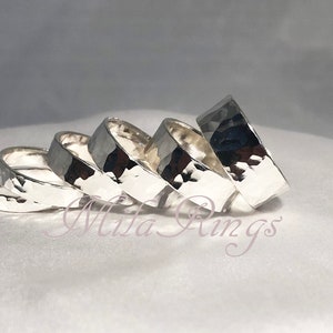 May include: Five silver hammered rings stacked on top of each other. The rings are all the same width and have a smooth, polished finish.
