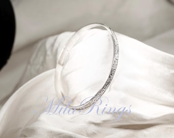 May include: A silver bangle bracelet with an intricate floral design around the edge.