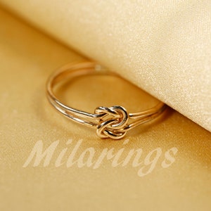 May include: A gold knot ring with a simple design. The ring is made of two bands of metal that are twisted together to form a knot.