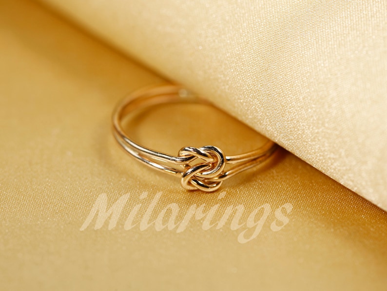 May include: A gold knot ring with a simple design. The ring is made of two bands of metal that are twisted together to form a knot.