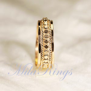 May include: A gold band ring with a textured design featuring multiple rows of small circles.