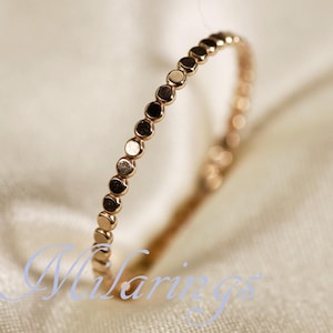 May include: A delicate rose gold ring featuring a series of small, evenly spaced circular accents. The ring is set against a soft, off-white background, highlighting its polished finish and minimalist design. The ring's design is simple and elegant.