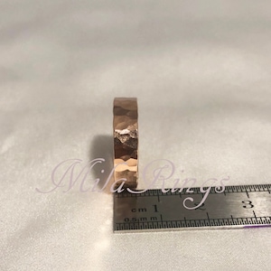 May include: A hammered gold band ring with a textured surface. The ring is measured against a ruler, showing it is approximately 1 cm wide.