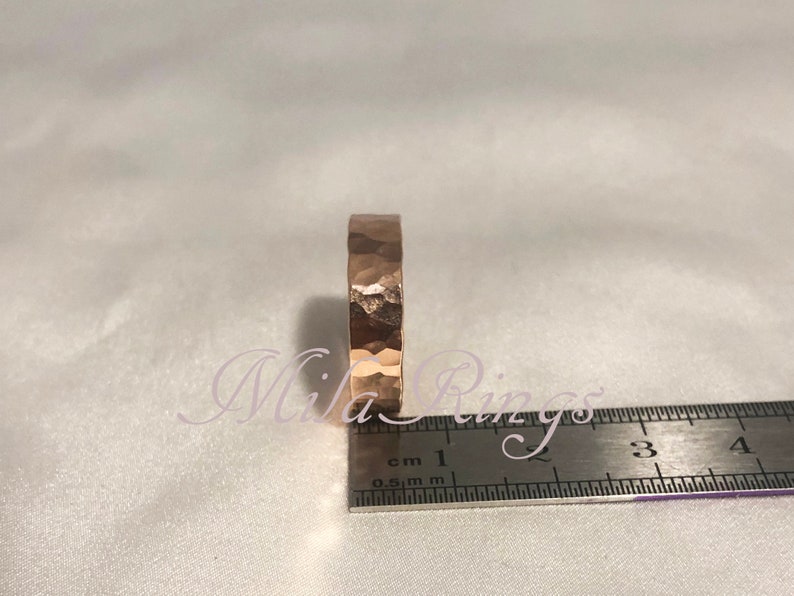 May include: A hammered gold band ring with a textured surface. The ring is measured against a ruler, showing it is approximately 1 cm wide.