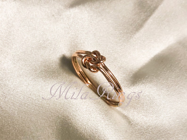 Op de afbeelding: Een knoop ring van ros&eacute;goud met een eenvoudig ontwerp. De ring is gemaakt van twee draadbanden die samen gedraaid zijn om een knoop te vormen.