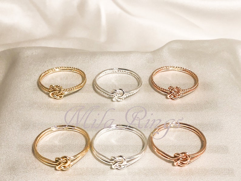 Op de afbeelding: Zes gouden, zilveren en ros&eacute;gouden ringen met een knoopdesign. De ringen zijn allemaal in dezelfde stijl, maar in verschillende kleuren.
