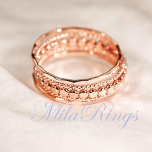 Puede incluir: Un anillo de oro rosa con un dise&ntilde;o apilado de tres bandas distintas. La banda superior es lisa y ondulada, la banda central est&aacute; trenzada y la banda inferior consiste en una serie de peque&ntilde;as cuentas circulares elevadas. Texto Mila Rings visible.