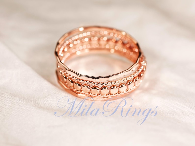Puede incluir: Un anillo de oro rosa con un dise&ntilde;o apilado de tres bandas distintas. La banda superior es lisa y ondulada, la banda central est&aacute; trenzada y la banda inferior consiste en una serie de peque&ntilde;as cuentas circulares elevadas. Texto Mila Rings visible.