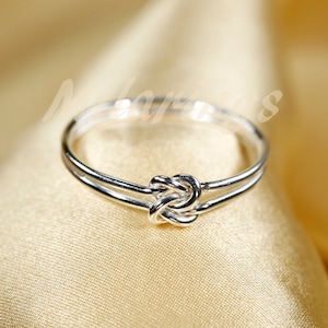 May include: A silver ring with a knot design. The ring is simple and elegant.