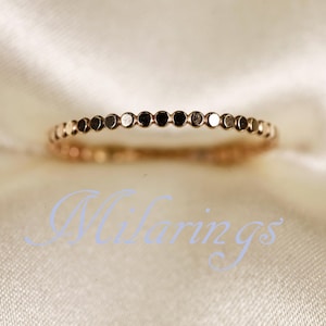 May include: A delicate rose gold ring featuring a series of small, evenly spaced circular accents. The ring is set against a soft, off-white background, creating a subtle contrast. The ring's design is simple and elegant.