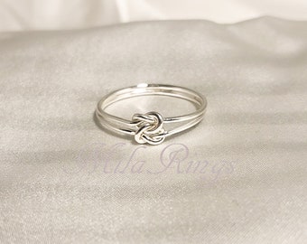 May include: A silver ring with a knot design. The ring is made of two bands of silver that are intertwined.