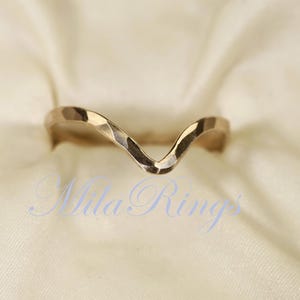 May include: A gold-toned, hammered metal ring with a V-shaped design. The ring is open at the top and has a textured finish.
