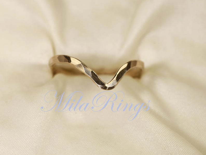 May include: A gold-toned, hammered metal ring with a V-shaped design. The ring is open at the top and has a textured finish.