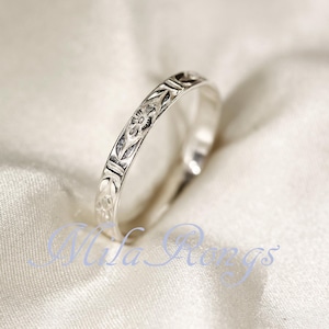 Könnte beinhalten: Ein silberner Ring mit einem eingravierten Blumenmuster. Der Ring ist vor einem weißen, strukturierten Hintergrund platziert. Das Design des Rings umfasst kleine Blumen und geometrische Formen. Der Ring ist im Bandstil gehalten, und die Gravur verläuft rundherum.