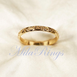 May include: A gold wedding band with a delicate, intricate floral design.