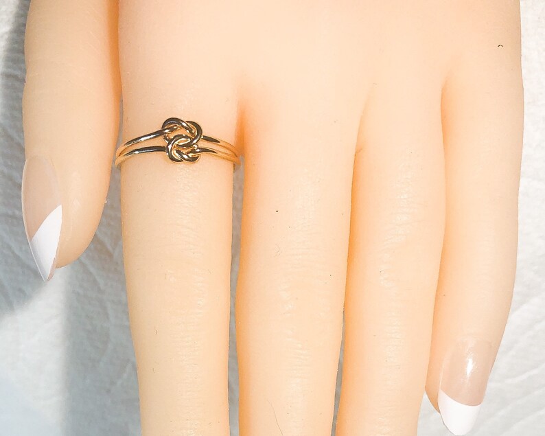 May include: A gold knot ring with a simple design. The ring is worn on a model's finger.